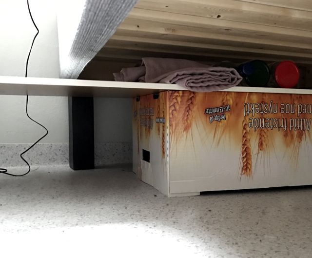 Blick unter ein Bett, Holzplatte auf Karton als Tisch