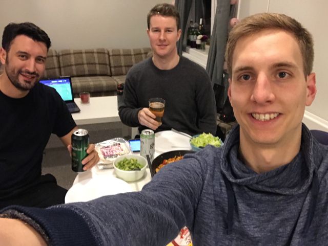 drei Männer stoßen mit Bier an, Essen auf Küchentisch