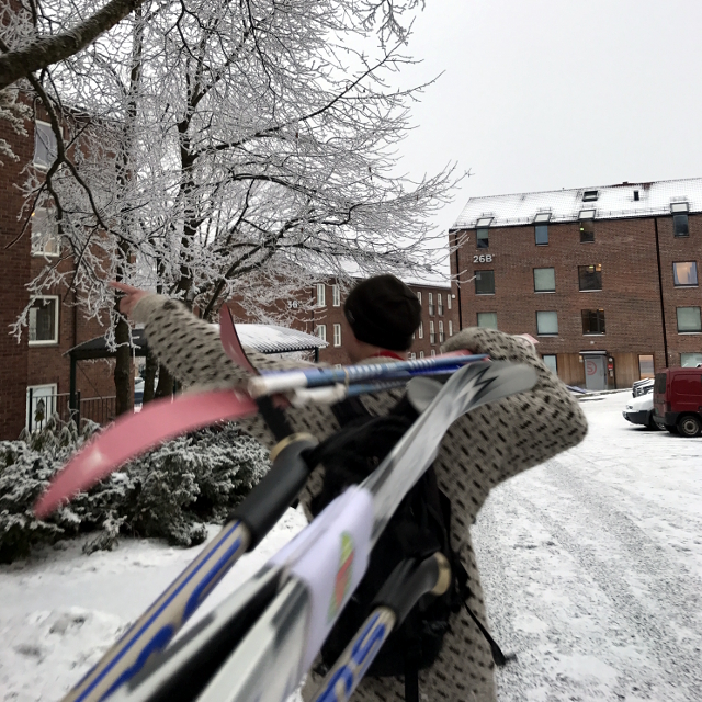 Mann mit Skiern geschultert vor Wohnhäusern