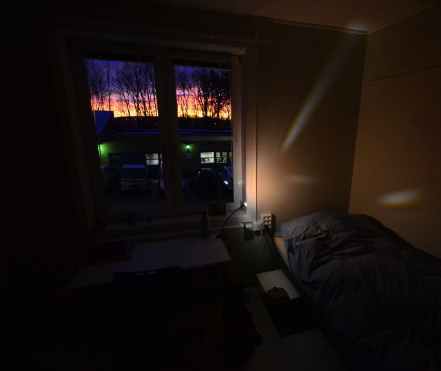 dunkler Raum mit Schreibtisch, Blick durchs Fenster auf den Sonnenaufgang