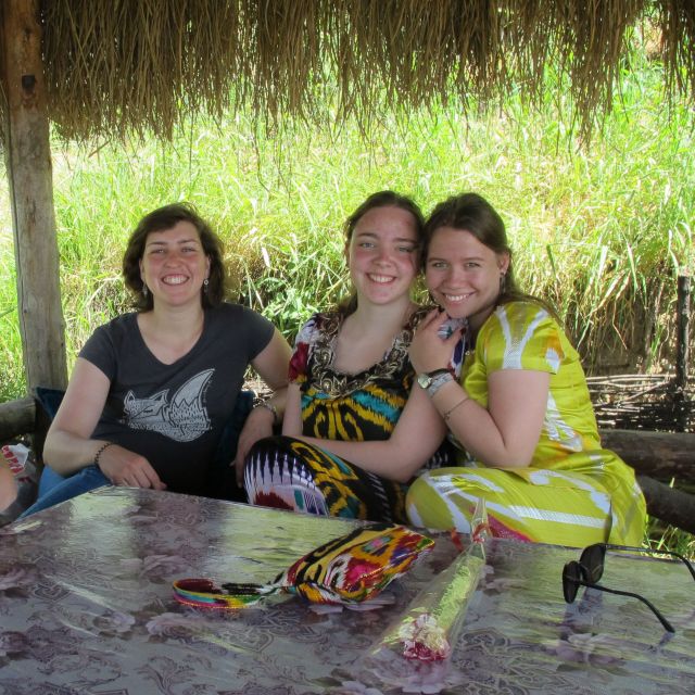 Drei Frauen auf einer Terasse, zwei davon in Atlasgewändern, eine in westlicher Kleidung.