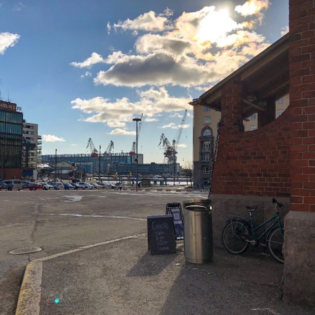 Szenerie am Hafen: Blauer Himmel, ein paar Wolken. Im Hintergund Hafenkrähne, rechts im Vordergrund ein Backsteingebäude