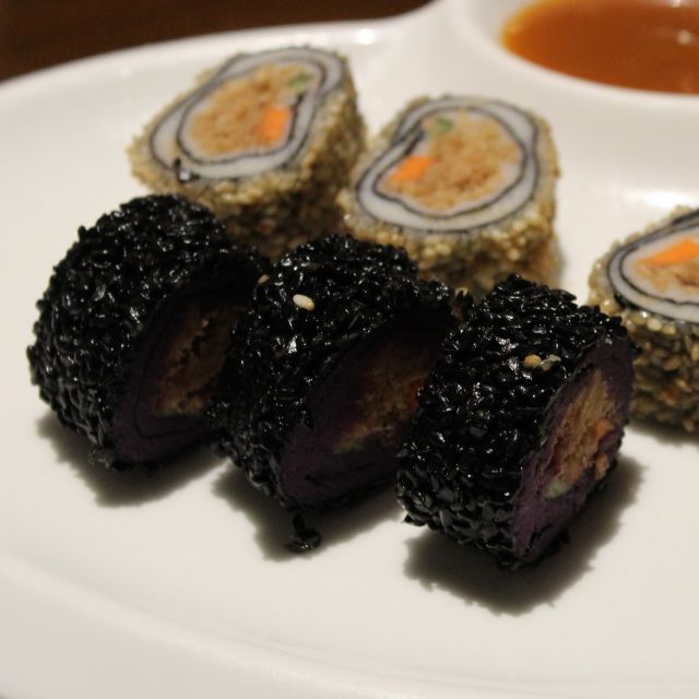 Das Bild zeigt einen weißen Porzellanteller mit Sushi. Das Sushi ist mit schwarzem bzw. weißem Sesam ummantelt.
