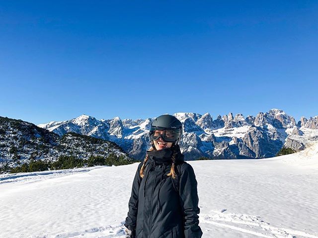 Studentin Carina steht auf einem Berggipfel in den italienischen Bergen. Sie trägt eine Snowboard-Ausrüstung und lacht.