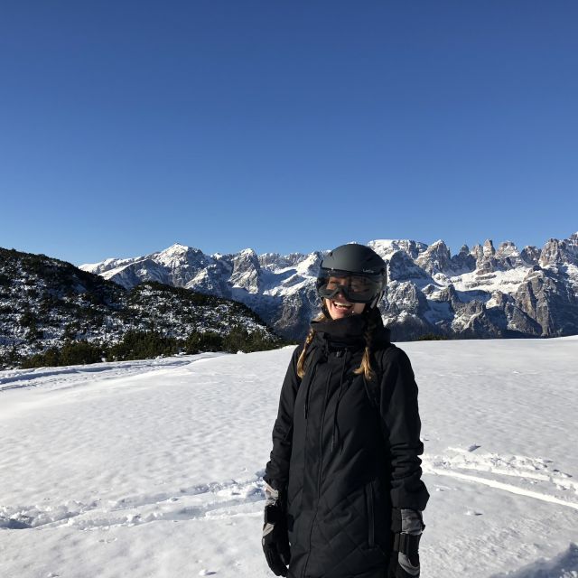 Studentin Carina steht lachend in Snowboardmontur auf einem verschneiten Berg.