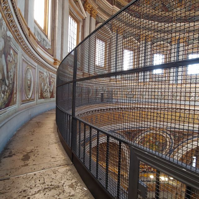 Der Weg im Inneren der Kuppes des Petersdoms, rechts ein hoher Zaun, links Mosaike