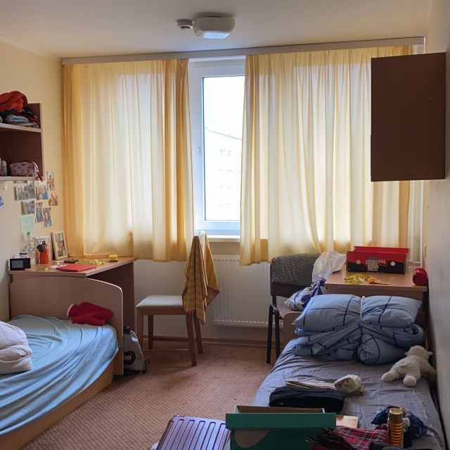 Helles Zimmer mit zwei Betten und gelben Gardinen.
