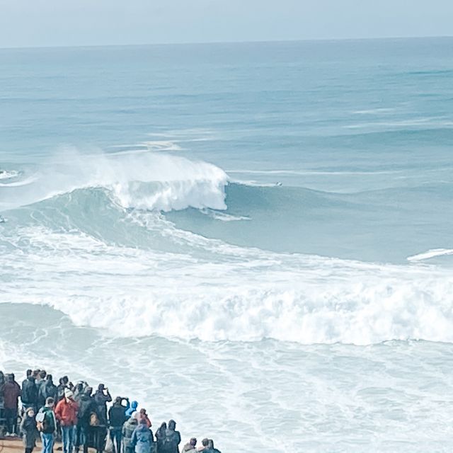 Blick auf eine groé Wellen mit menschen im Vordergrund.