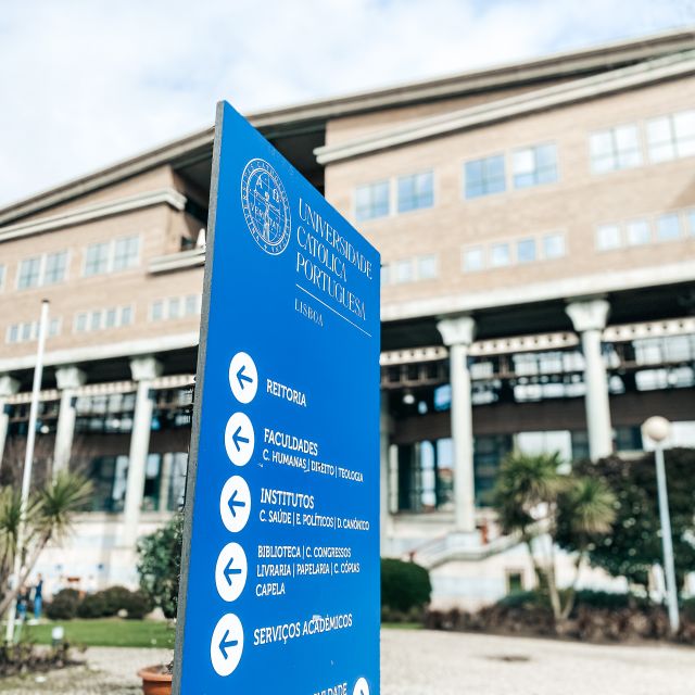 Blaues Schild der Universidade Católica Portuguesa vor Unihauptgebäude.