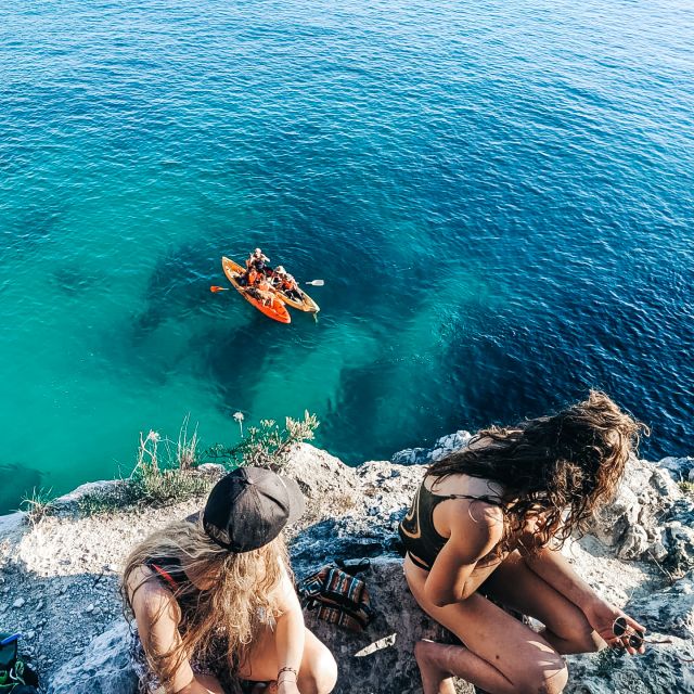 Zwei Frauen auf einem Fels, im Hintergrund das Meer und zwei Kayak-Boote.
