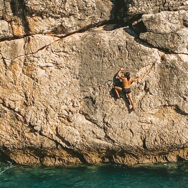 Mann klettert ohne Sicherung am Fels über dem Meer.