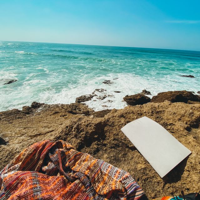 Jacke und Schreibblock auf Felsen, im Hintergrund das Meer.