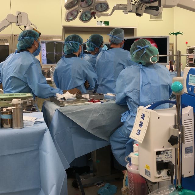 vier Chirurgen in blauer OP-Kleidung und Kittel beim Operieren. 