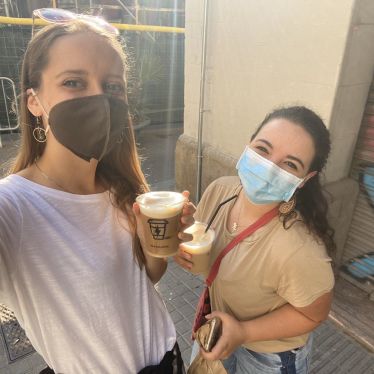 Zwei Mädchen mit Masken und Kaffee in der Hand.