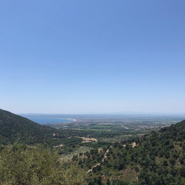 Cea34fae-4b56-40e2-a4f2-5db54b7b7f97 Ausblick über eine hügelige Landschaft, mit dem Meer im Hintergrund.