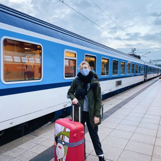 Person steht mit Koffer vor einfahrendem Zug am Gleis