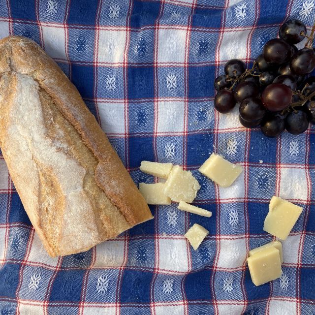 Auf einem Küchentuch liegen Baguette, Käse und Weintrauben