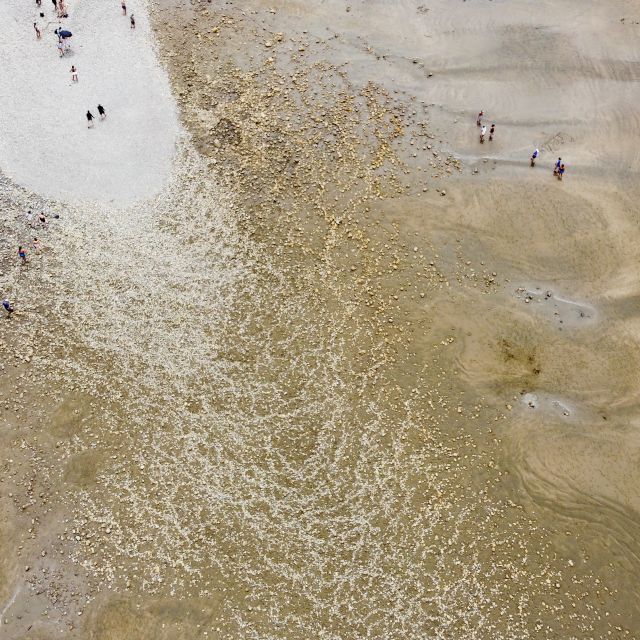 Luftaufnahme des Strandes, man sieht steinige Strukturen und kleine Menschengruppen.