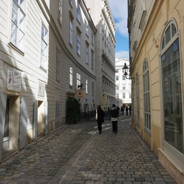 Gasse mit Kopfsteinpflaster, links und rechts alte Häuser, in der Mitte sind zwei Frauen von Hinten zu sehen, die hier entlang spazieren.