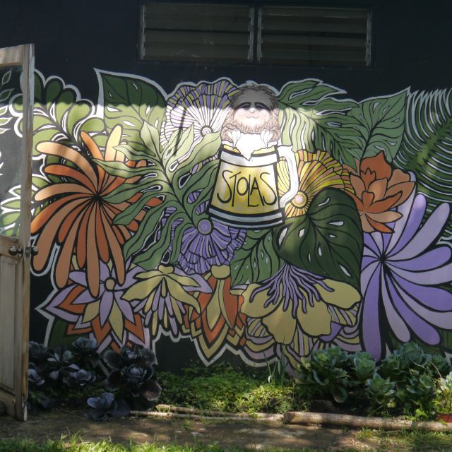 Eine Außenwand mit einem großen Mural mit Blättern, Blüten, einem Bierkrug und einem Faultier.