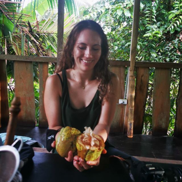Carla sitzt an einem Tisch und hält eine aufgeschnittene Kakaofrucht in der Hand.