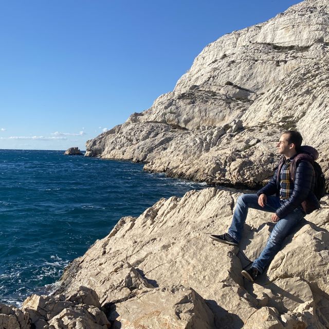 Mann sitzt auf Kliffen, im Hintergrund das Meer