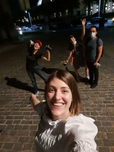 Eine junge Frau in weißem Oberteil macht ien selfie mit drei Leuten die lustig im Hintergrund posieren