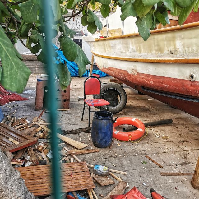 Ein roter Stuhl steht hinter einem grünen Zaun neben einem Boot, das wohl neu angestrichen wird.