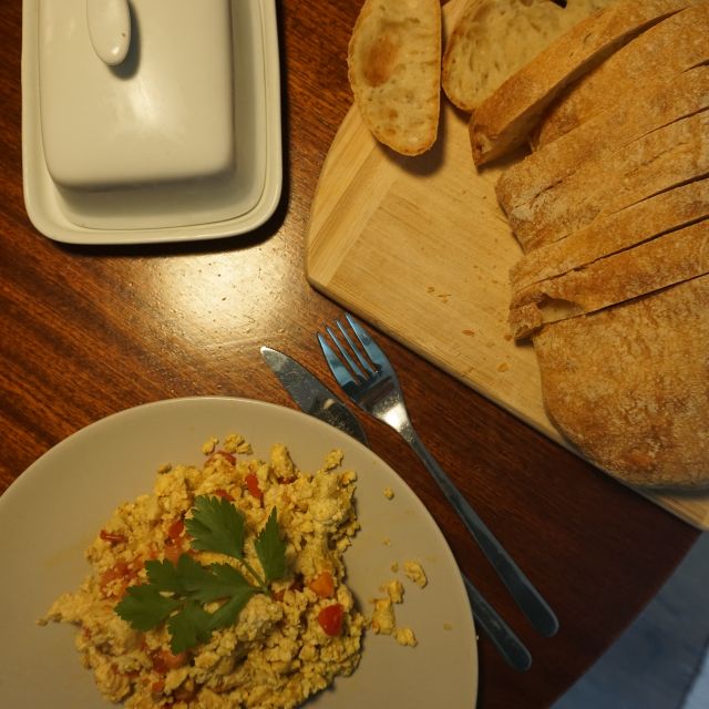 Teller mit gelber Masse und Holzbrett auf dem Weißbrot liegt. Butterdose links im Bild. Alles steht auf einem unklen Holztisch.