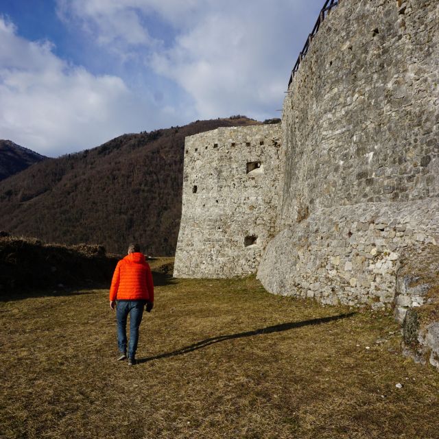 Rechts im Bild sind alte Steinmauern zu sehen. Ein Mann in lechtend roter Jacke geht hier entlang.