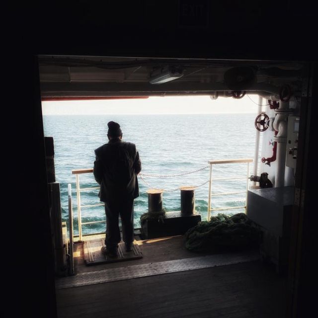 Mann steht auf der Fähre und blickt aufs Meer.
