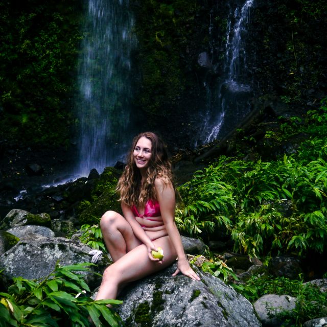 Carla sitzt auf einem Stein vor einem großen Wasserfall im Grünen