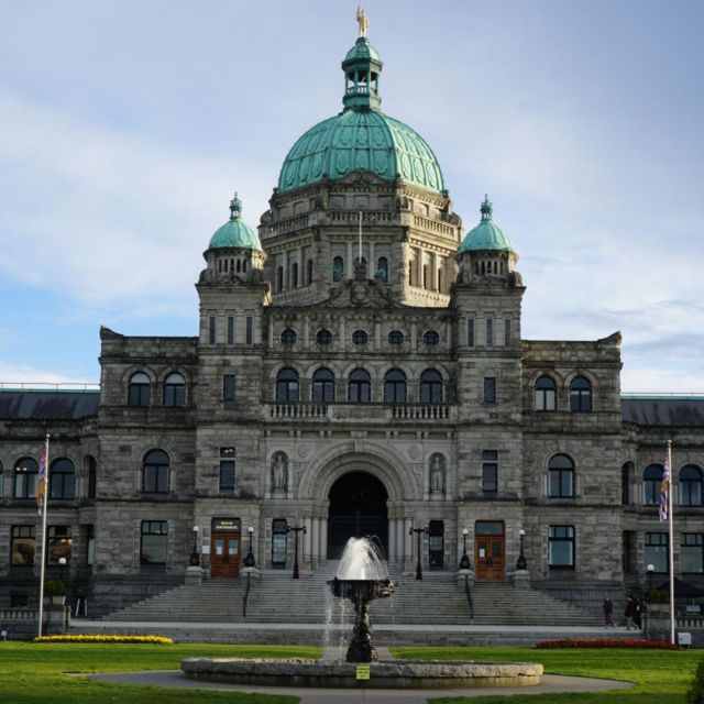 Das Parlament von British Columbia. Ein altes Gebäude mit blauen Dächern, imposanter Treppe und einem Brunnen im Park