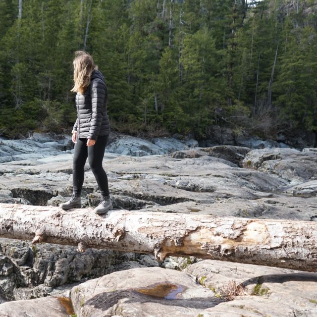 Mädchen steht auf einem Baumstamm. Im Hintergrund ein Felsenmeer und ein reßender Fluss sowie Nadelbäume