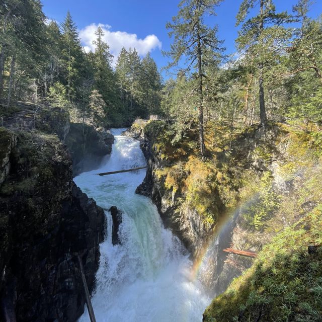 Wasserfälle, hellblauer Himmel, ein Regenbogen in der rechten unteren Ecke, der Wasserfall ist umgeben von wunderschöner Natur