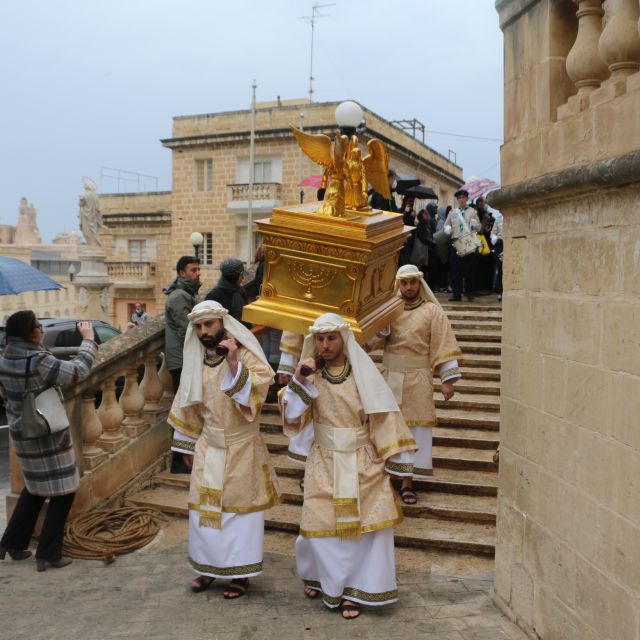 Vier verkleidete Männer tragen einen goldenen Schrein eine Treppe herunter.