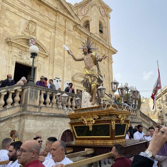 Männer in weißen Gewändern tragen eine Jesus Statue vor einer Kirche.