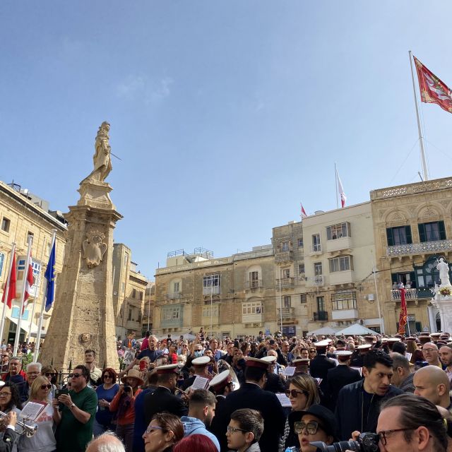 Ein Platz gefüllt mit Menschen, im Hintergrund weht eine große maltesische Flagge.