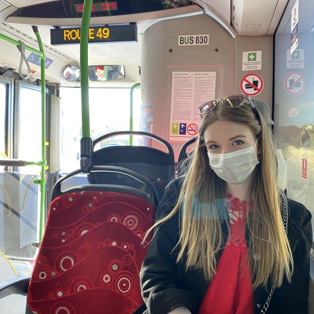 Ein Mädchen mit Maske sitzt auf einem roten Sitz im Bus.