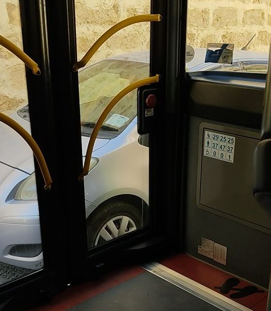 Eine Bustür, hinter der sehr nah ein silbernes Auto geparkt ist