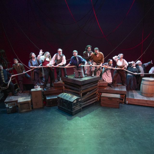 Der gesamte Cast befindet sich auf den Plattformen des Bühnenbildes und hält ein Seil.