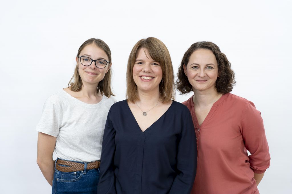 Gruppenfoto mit drei Frauen vor einem weißen Hintergrund