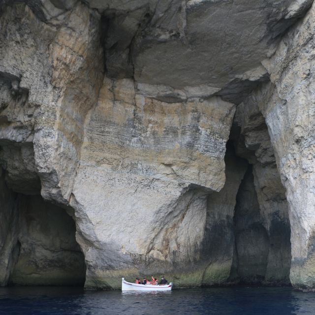Ein kleines Boot mit Menschen fährt durch große Höhlenformationen. Die Felsen weisen einen Farbverlauf auf.