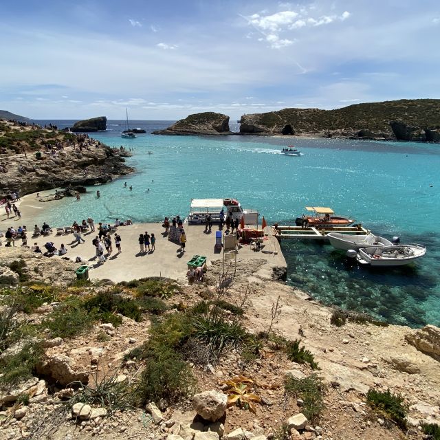 Eine Ansammlung von Touristen am felsigen Strand. Auf dem türkisen und glasklaren Wasser fahren mehrere Boote und im Hintergrund sind einige Felsformationen zu erkennen.