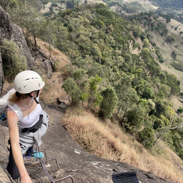Ausblick von einem Felsen. Ein Mädchen mit Helm und Klettergurt gucckt in die Landschaft.