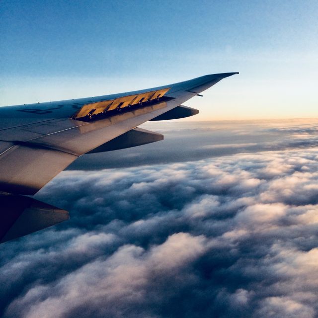 Flügel eines Flugzeuges aus dem Flugzeug heraus fotografiert. Im Hintergrund Wolken