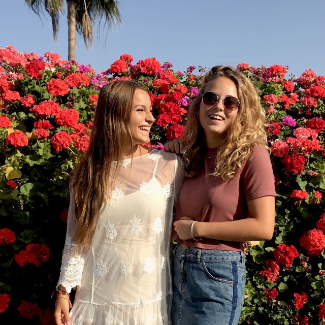 zwei lächelnde Mädchen, Palme und eine Menge roter Blüten im Hintergrund