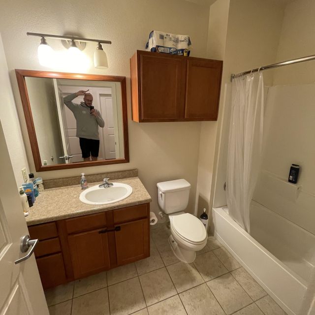 Zusehen ist mein kleines Badezimmer mit braunen Möbeln. Ich stehe in einem studieren weltweit Pullover vor dem Spiegel und zeige das Peace Symbol.