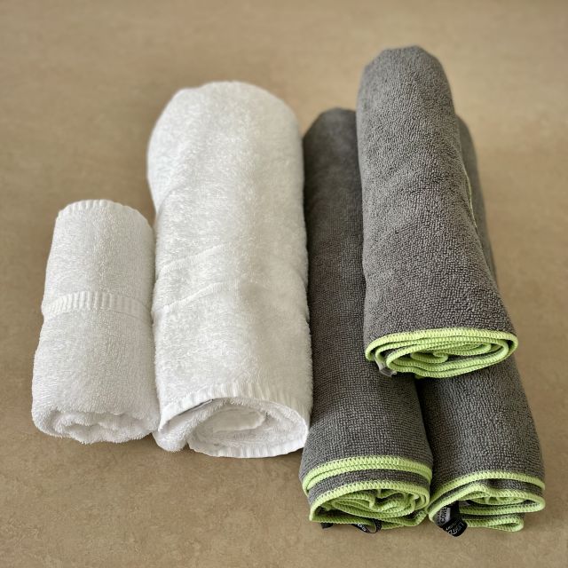Man sieht zusammengerollte Baumwoll- und Mikrofaser Handtücher. Es wird deutlich, dass Mikrofaser Handtücher weniger Platz in Anspruch nehmen.