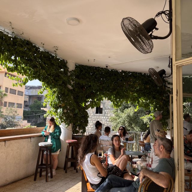 Menschen sitzen an Tischen in einem Außencafé, das mit Pflanzen bewachsen ist.